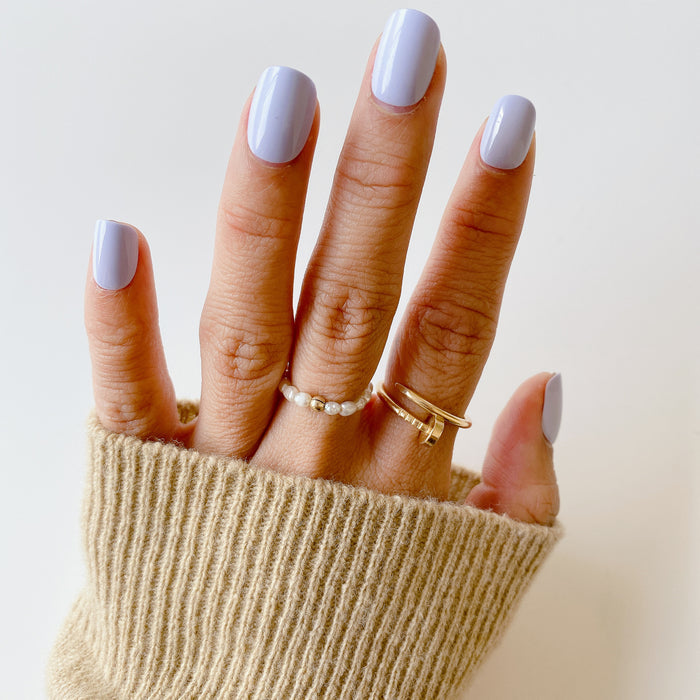 Hand wearing BP - Press-On | Extra Short | Squoval icy light blue false nails with gold and pearl rings and beige sweater sleeve