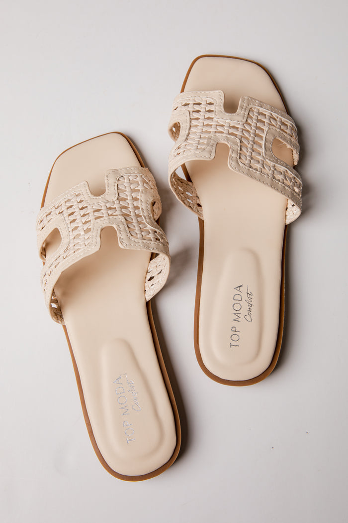 Pair of beige sandals with woven straps on a light gray background
