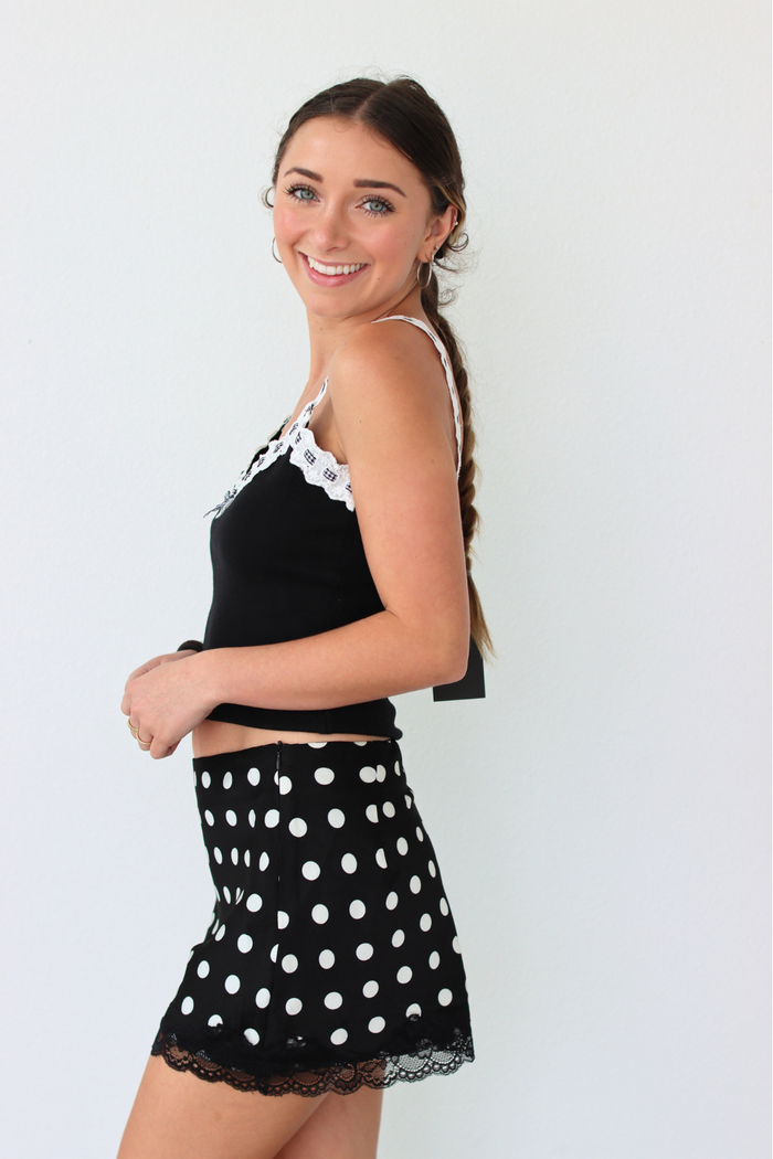 Woman wearing a black top with lace trim and a black polka dot skirt on a white background
