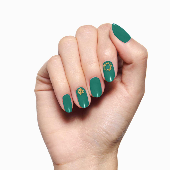 Hand with green polish and gold snowflake and wreath designs using O&J Cozy Lodge Nail Art Stickers for winter mani