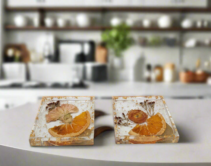 Square pressed flower coasters with preserved orange peel slices on a kitchen countertop