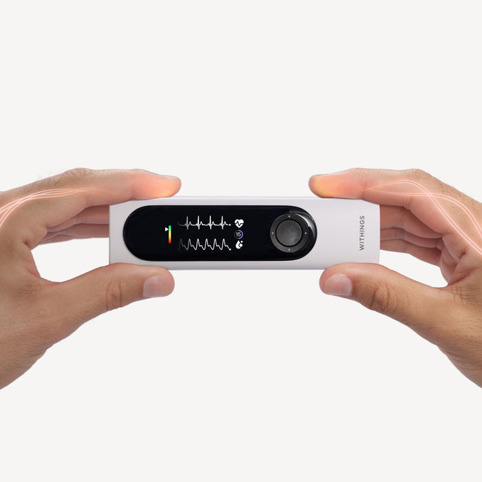 Withings BeamO — Beam-O — Device held horizontally with both hands, ECG screen lit, white background, stylized light on fingers — two hands, active screen, handheld