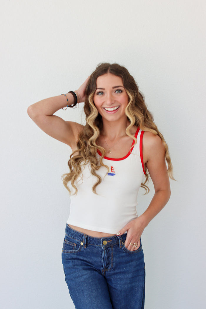 Woman wearing a white tank top with red trim and blue jeans against a white background