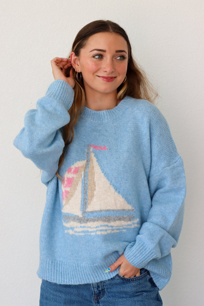 Woman wearing a light blue sweater with a sailboat design against a white background