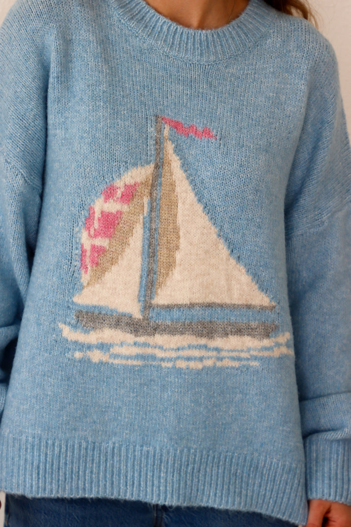 Blue sweater with a sailboat design on a neutral background