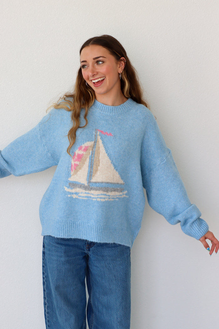 Woman wearing a light blue sweater with a sailboat design against a white background