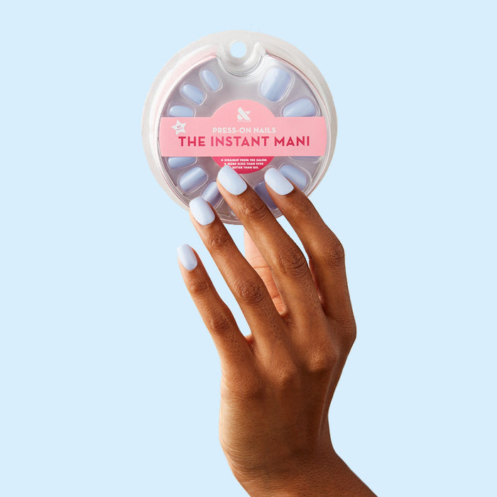 Hand with BP - Press-On | Extra Short | Squoval nails in icy light blue holding packaged press-on nails against pale blue background