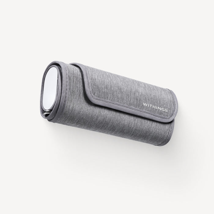 Withings BPM Connect — Connected blood pressure cuff — Three-quarter view on white background, rolled cuff with silver oval display and Withings logo — grey, compact, fabric