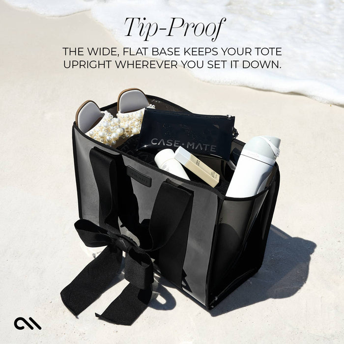 Black tote bag with items on a sandy beach, featuring text about its tip-proof design.