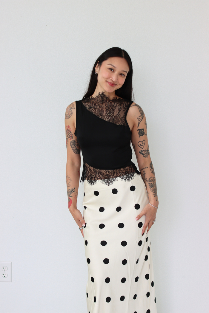 Woman wearing a black lace top and white polka dot skirt against a plain background