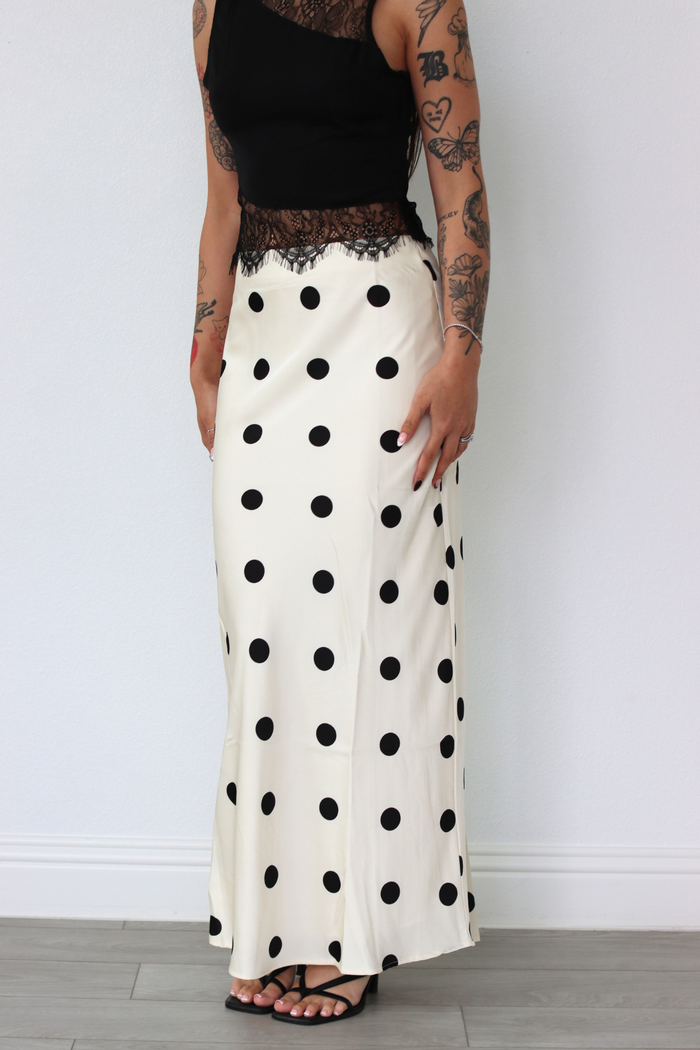 Person wearing a black top and white polka dot skirt against a plain background