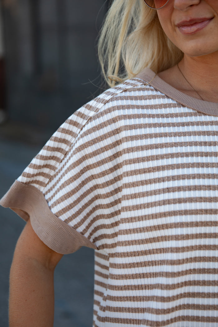 A close-up of a woman wearing a brown and white horizontally striped short-sleeve waffle-knit top with solid brown ribbed trim.