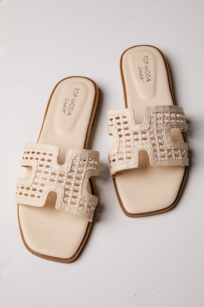 Pair of beige sandals with decorative straps on a light gray background