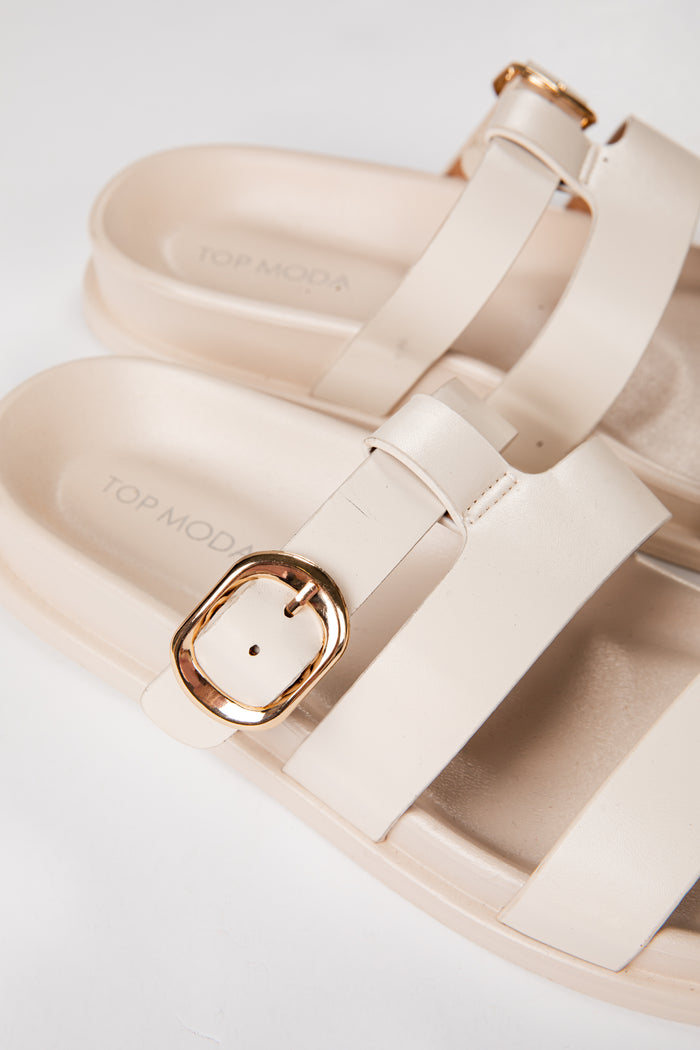 Beige sandals with gold buckles on a light background