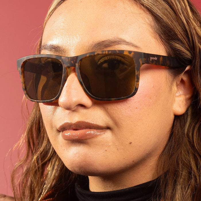 Close-up of a person wearing tortoiseshell sunglasses with a pink background