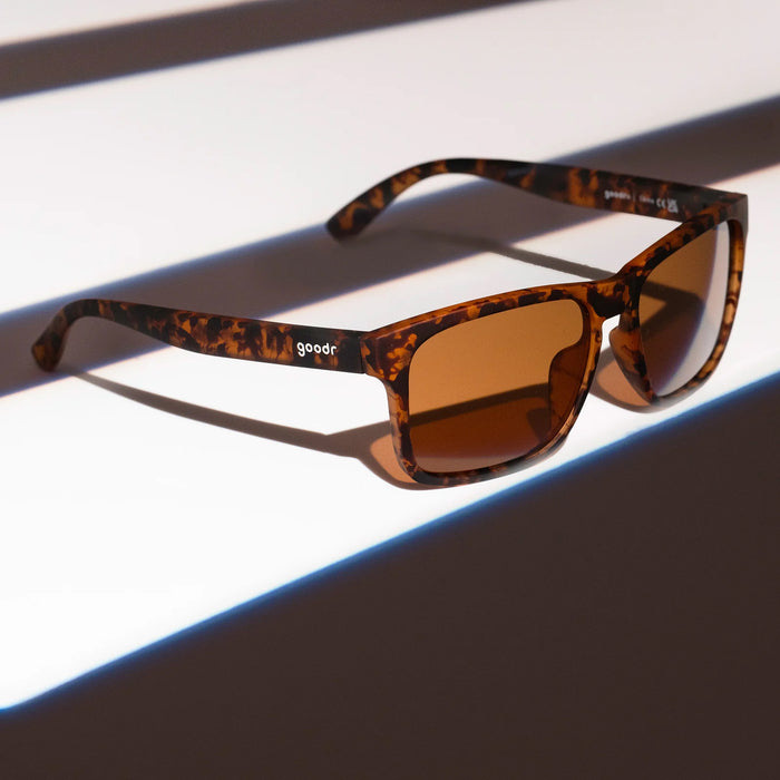 Sunglasses with tortoiseshell frame and brown lenses on a reflective surface