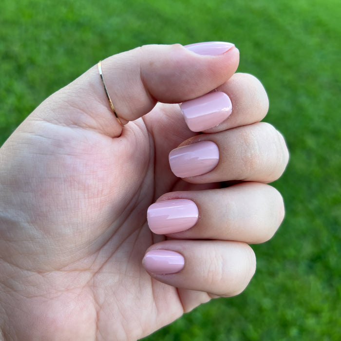 Hand with HZ - Press-On | Short | Squoval rosy neutral false nails displaying a soft feminine mani on natural skin tone outdoors