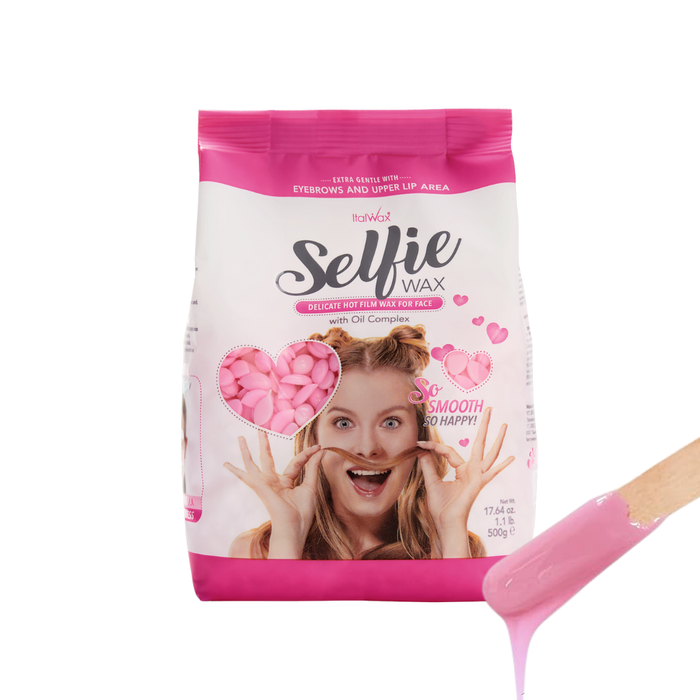 W390 Italwax 500g Selfie Delicate Film Wax | A bag of pink delicate Italwax Selfie Film Wax for facial hair removal and a wooden spatula with soft pink wax dripping