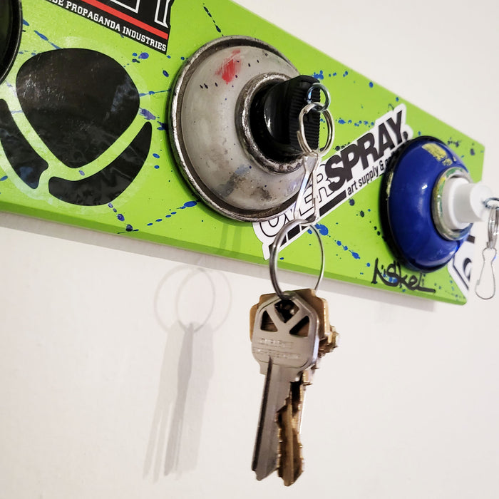 Wall mounted keychain holder with tops of aerosol cans and nozzles.
