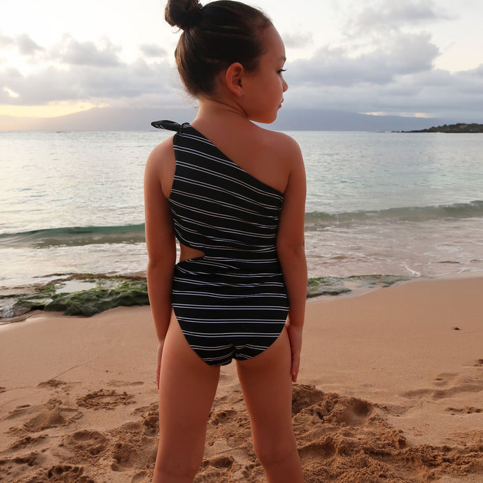 Young girl in a black and white striped swimsuit standing on a beach with ocean in the background