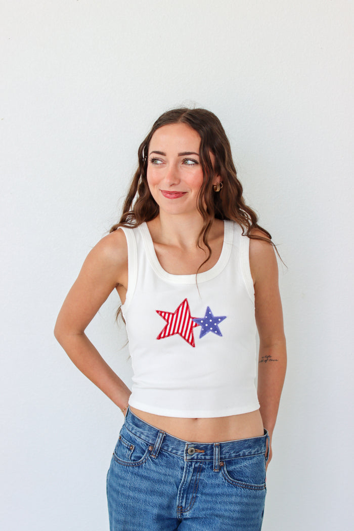 Woman wearing a white tank top with a star design on a plain background