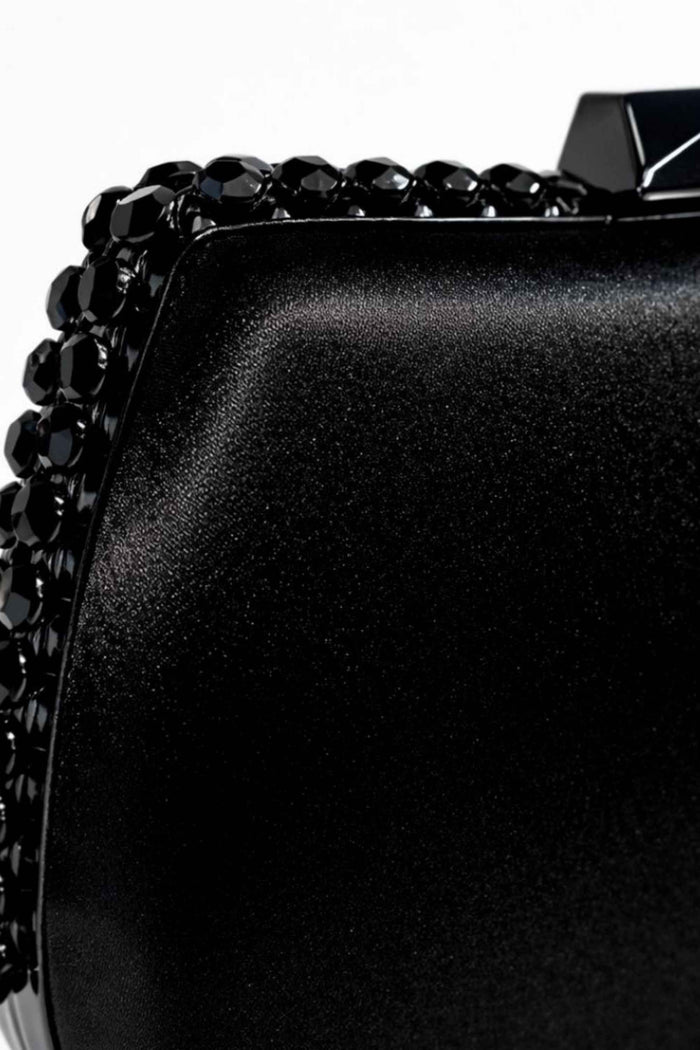 Close-up of a black satin clutch with a textured surface, adorned with black faceted beads along the edge, perfect for evening wear