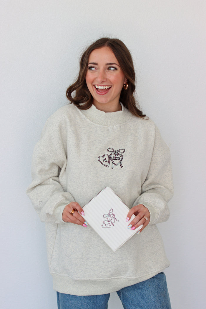 Woman wearing a light gray crewneck with a embroidery design against a white background