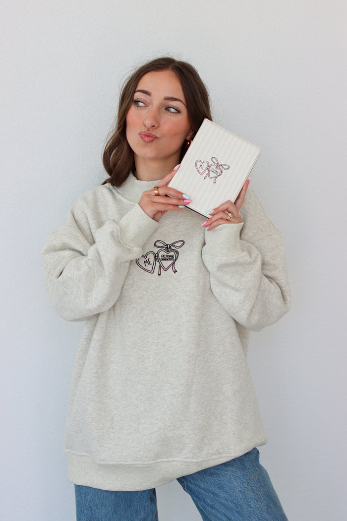 Woman wearing a light gray crewneck with a embroidery design against a white background