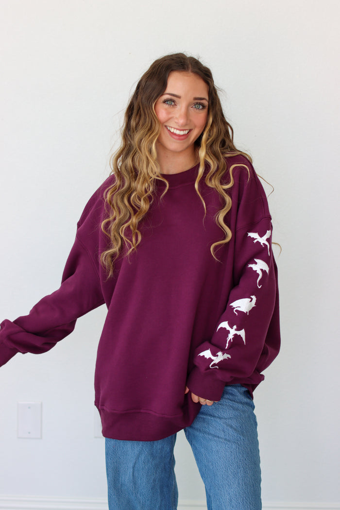 Woman wearing a purple crewneck with a embroidery design against a white background