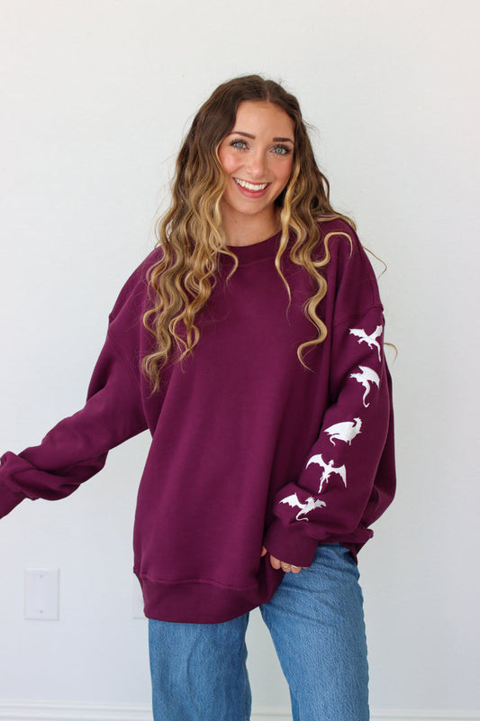 Woman wearing a purple crewneck with a embroidery design against a white background