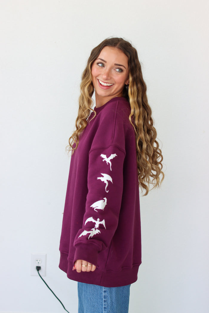 Woman wearing a purple crewneck with a embroidery design against a white background