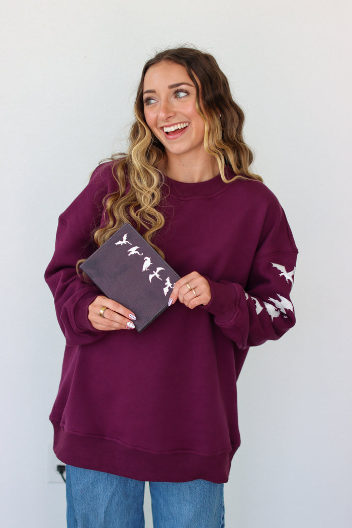 Woman wearing a purple crewneck with a embroidery design against a white background