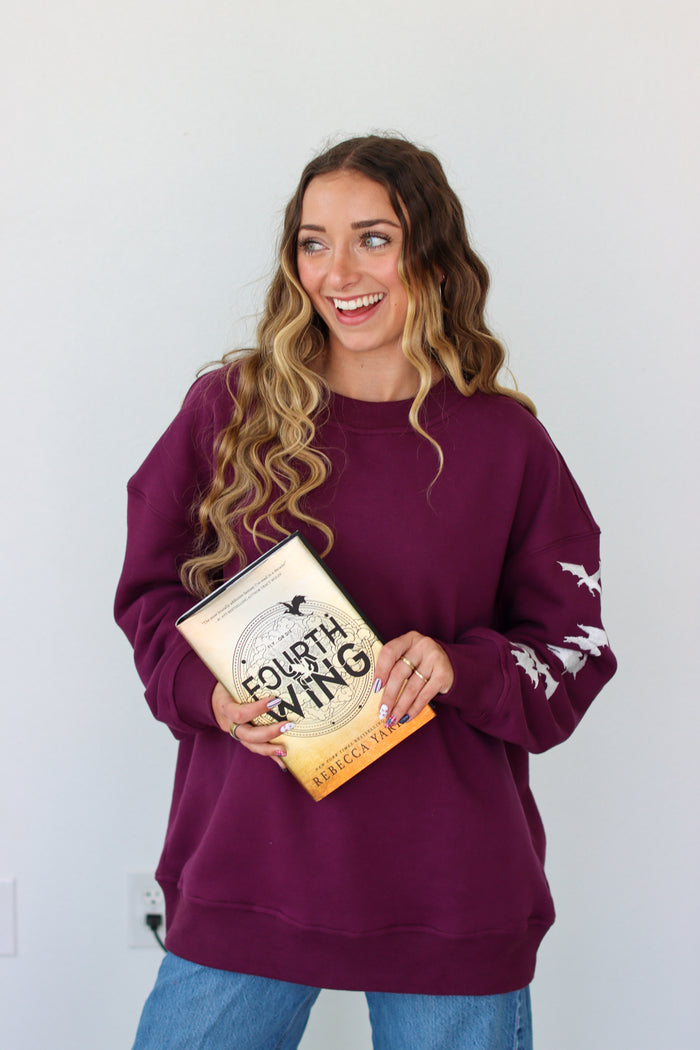 Woman wearing a purple crewneck with a embroidery design against a white background
