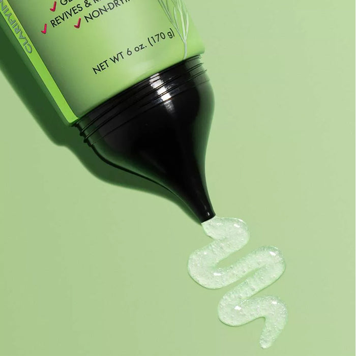 MIELLE rosemary mint scalp scrub tube dispensing green exfoliating gel with visible salt granules on green background