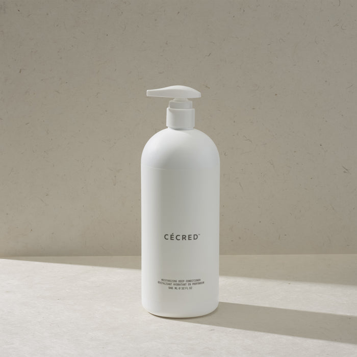 Cécred Moisturizing Deep Conditioner in the max size pump bottle, standing on a beige surface against a tan textured background