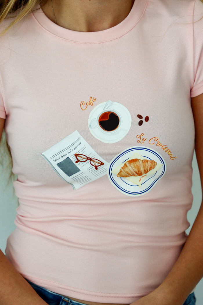 Pink t-shirt with coffee and croissant design worn by a person