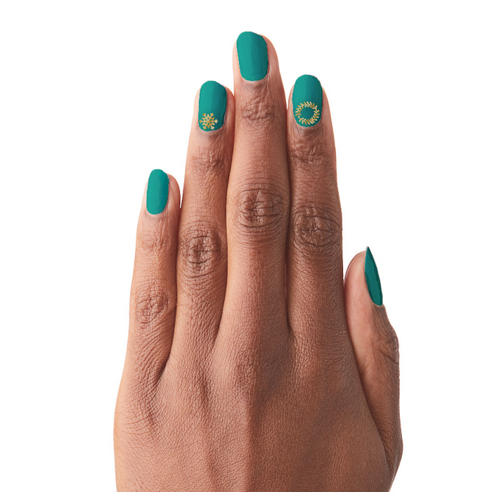 Hand with teal polish featuring delicate gold snowflake and wreath designs using O&J Cozy Lodge Nail Art Stickers