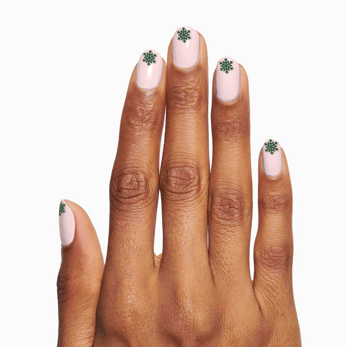 Hand with light pink polish and green snowflake designs using O&J Cozy Lodge Nail Art Stickers for winter manicures