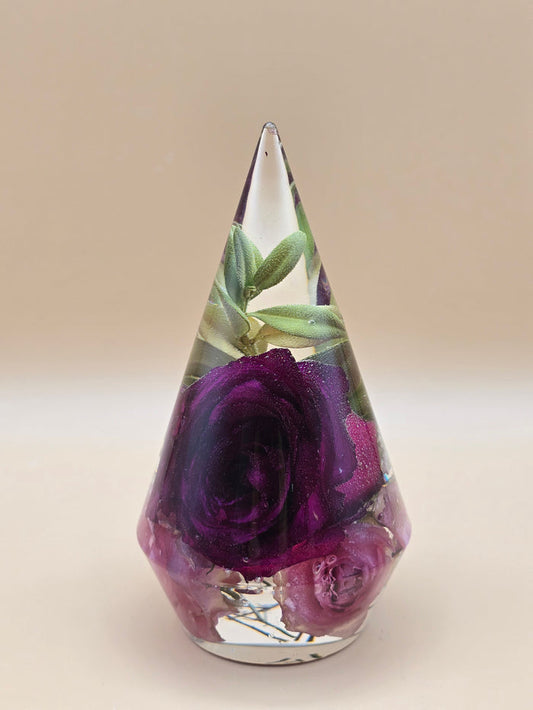Cone-shaped clear resin ring holder with preserved purple roses and green foliage, a wedding flower keepsake.