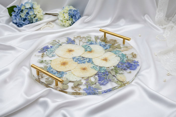 Wide landscape photo of a pressed flower 16-inch round resin tray with gold handles on a beige background