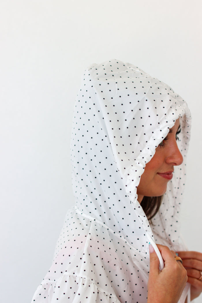 A woman wearing a white hood with small black polka dots, shown in profile against a plain white background.