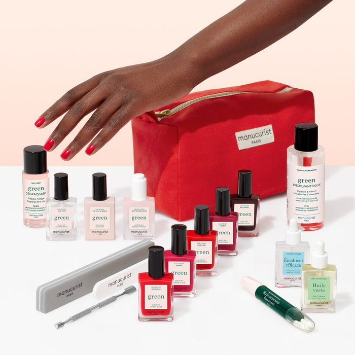 A hand with red nails reaches for the Manucurist Super Ultimate Kit—a red cosmetics bag filled with gel effect manicure essentials, polishes, files, clippers, oils, and tools—perfectly arranged for the ideal at-home manicure.