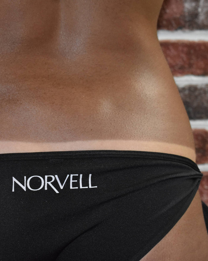 Person with a fresh Venetian Max tan wearing black Norvell bikini bottoms revealing a tan line.