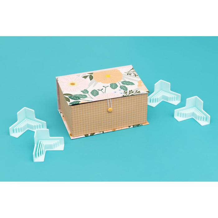 We R Memory - Corner Guides - 4/Pkg. Great for boxes, book covers, dioramas, and more! Holds corners tightly while adhesive sets. Works with 3mm, 2mm, 1.5mm, and 1mm wide chipboard. Imported. Available at Embellish Away located in Bowmanville Ontario Canada.