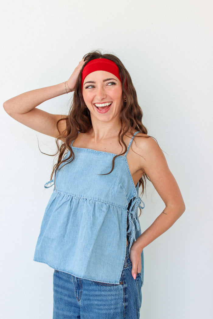 Woman wearing a light blue denim top and jeans with a red headband against a white background