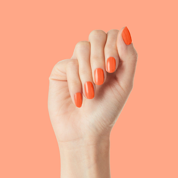 Hand with nails polished in bold tangerine "You're a 10" gel polish showing fresh and glossy manicure on coral background