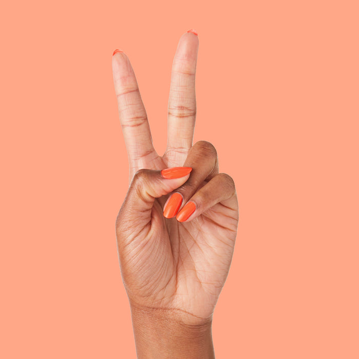 Hand with nails painted in bold tangerine You're a 10 gel polish showing fresh manicure on peach background